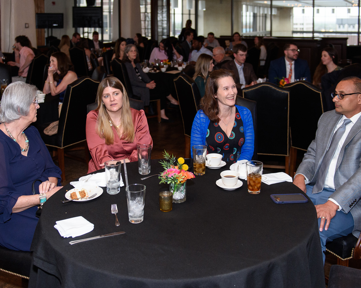 Four people are seated at a round table during a large event. Dr. Laura Tatpati is second from the right.